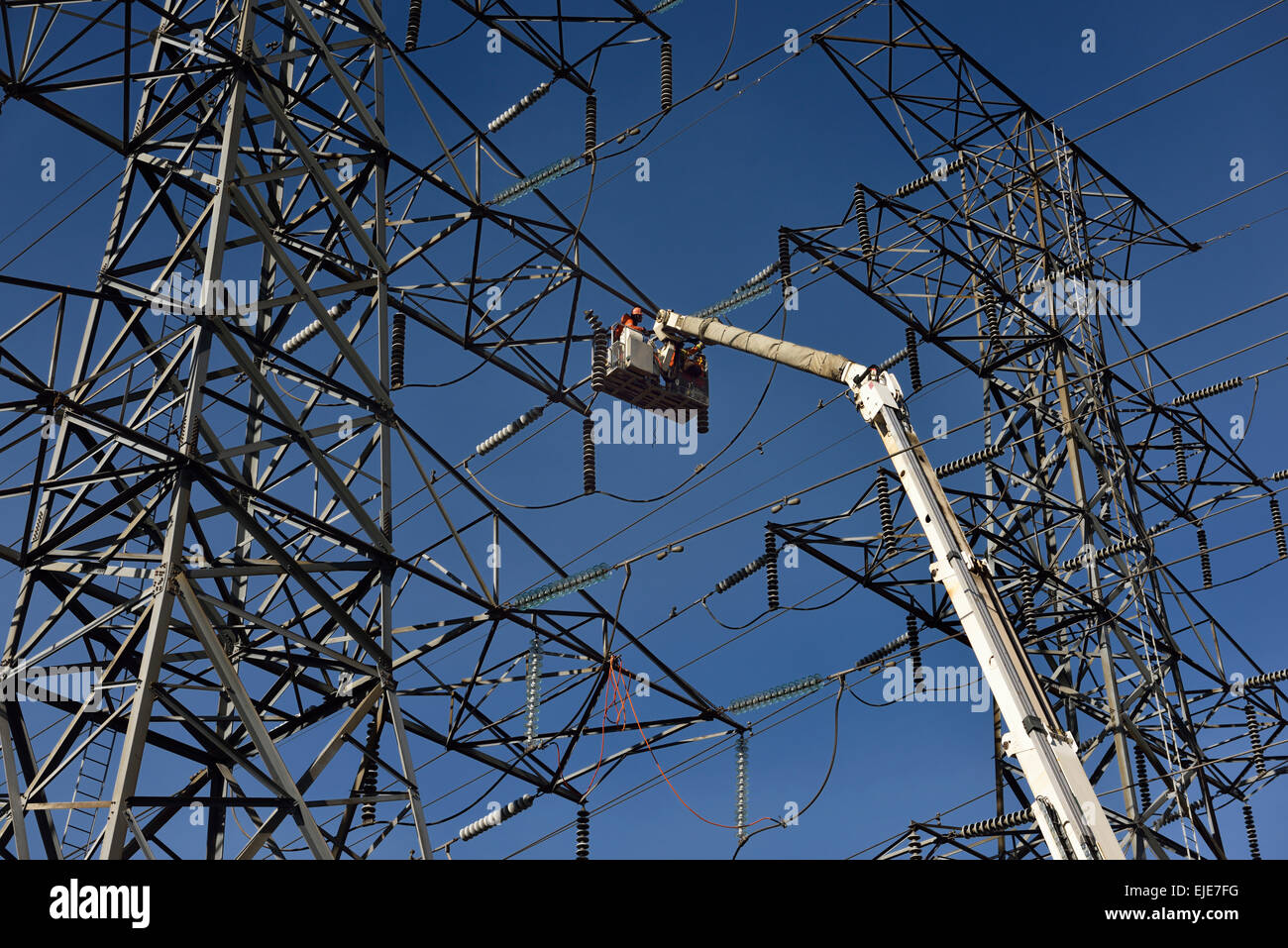 Hydro linemen on boom lift working to replace suspension insulators on high voltage electricity