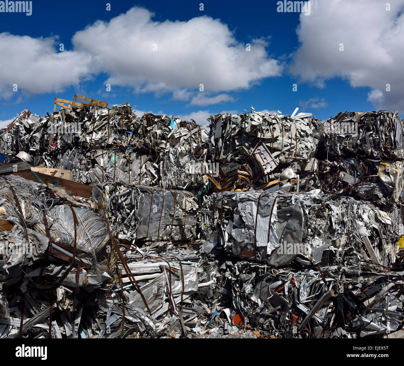 Mountain of crushed recycled scrap metal cubes with blue sky and clouds