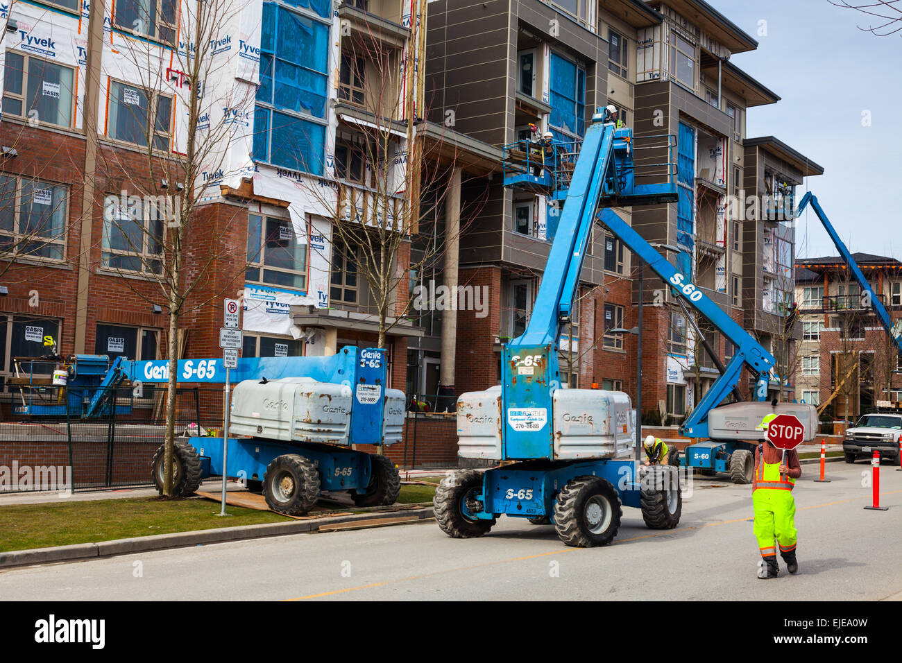 Four man-lift vehicles being used to apply exterior cladding to an apartment building Stock Photo
