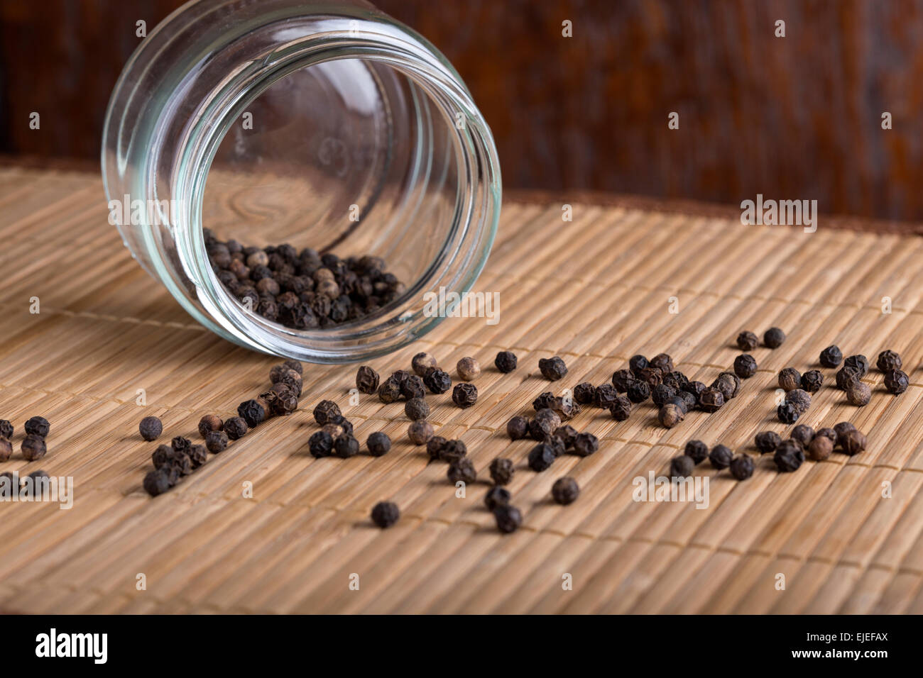 Black pepper in the inverted jar with glass on wooden background Stock Photo