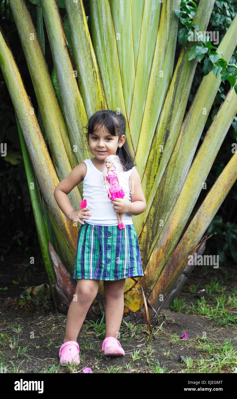 Girl, 4 years, holding a Barbie doll, posing in front of a palm tree, San Juan de Nicaragua or San Juan del Norte or Greytown Stock Photo