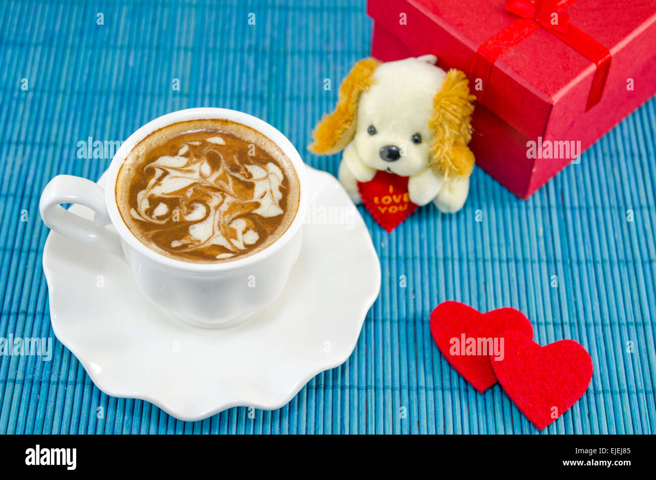 Artisan coffee in a white cup with decorated foam.  Red present box for Valentine's day, together with two hearts and a puppy do Stock Photo