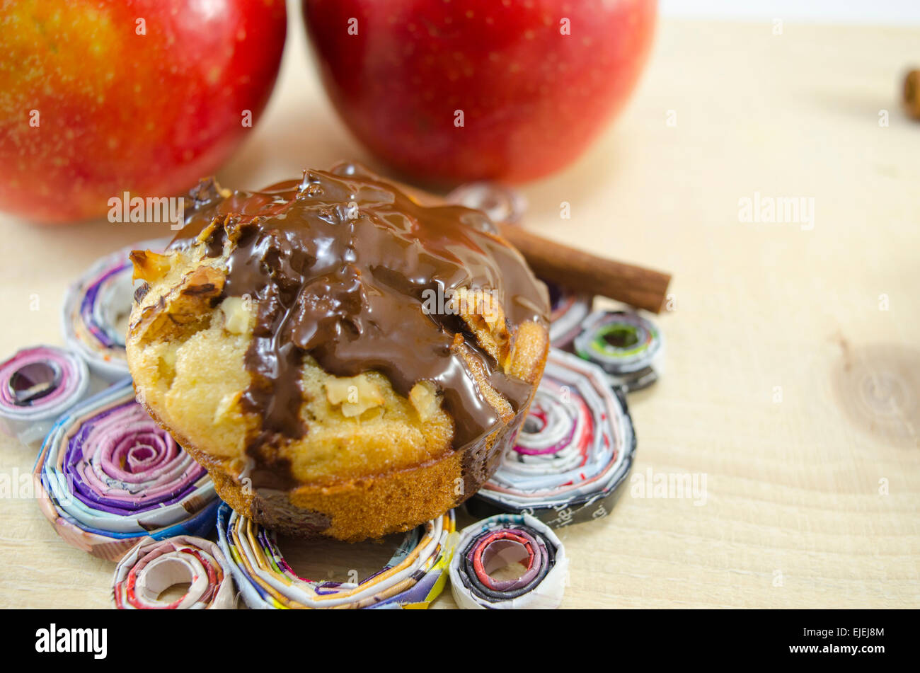 Delicious chocolate muffin standing on a hand made paper plate with two apples in the background Stock Photo