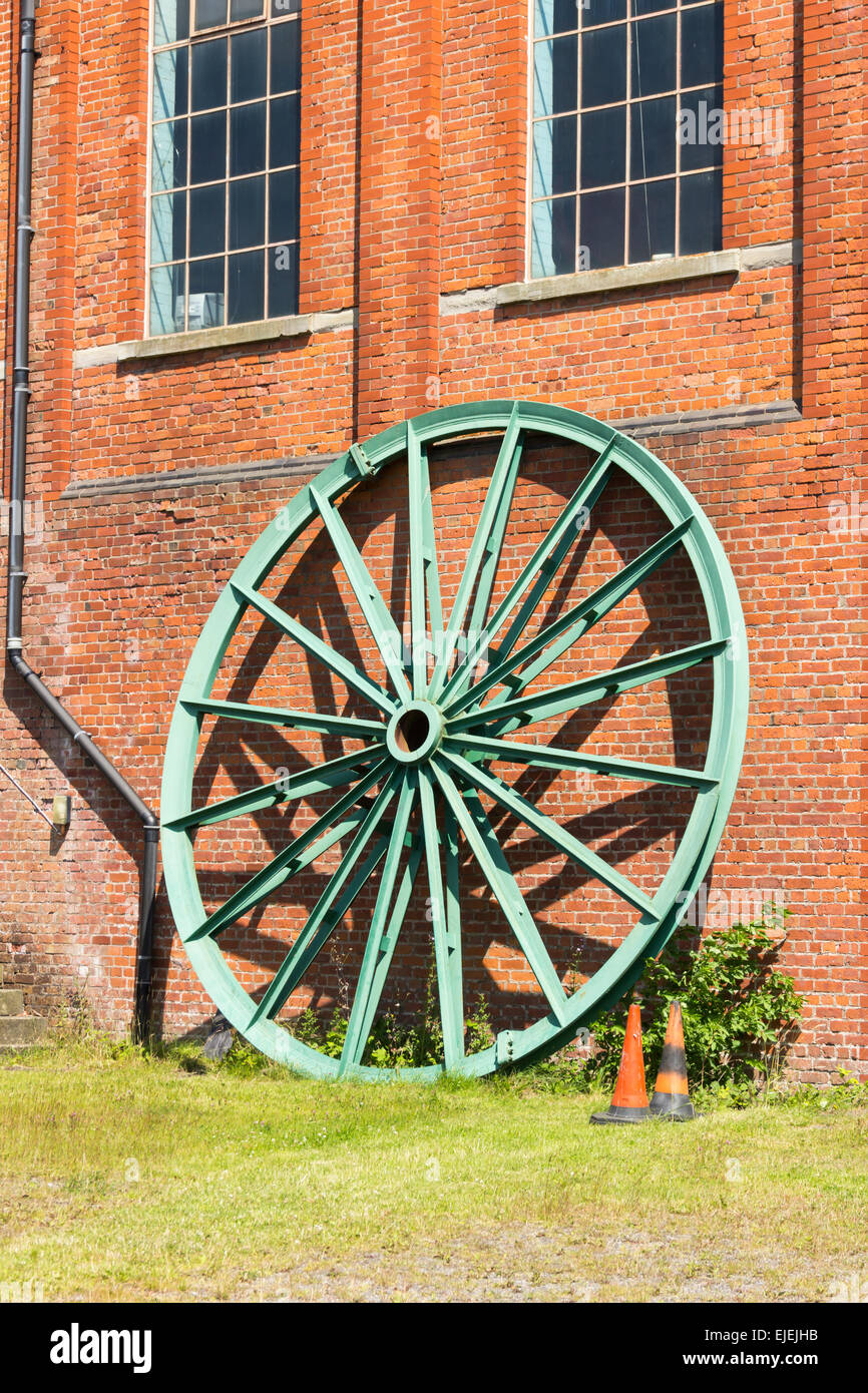 A large headgear pulley for the pithead winding gear, leaning against the engine house  at Astley Green Colliery Museum. Stock Photo