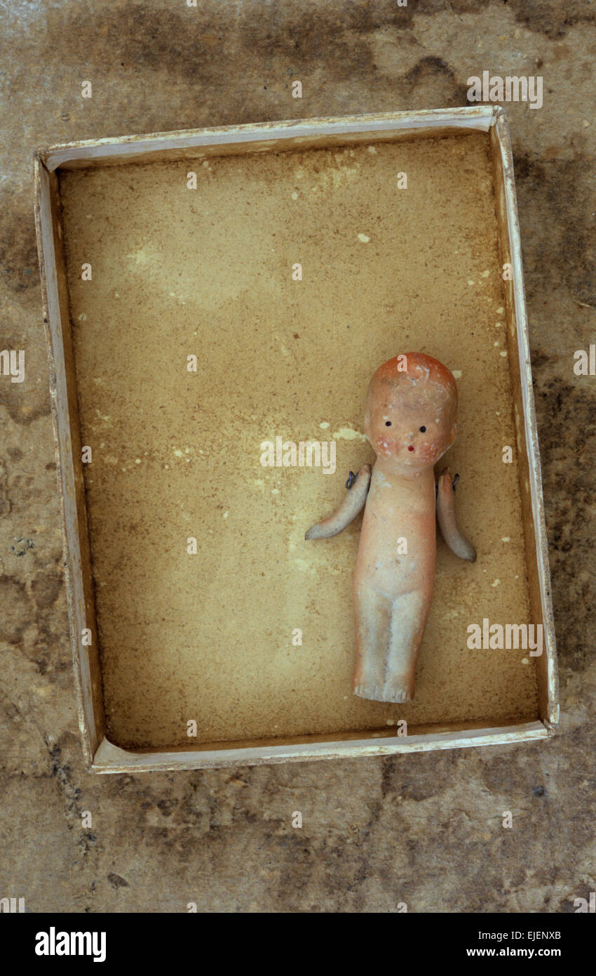 Small vintage bisque doll with wired arms lying in card tray on stained board Stock Photo