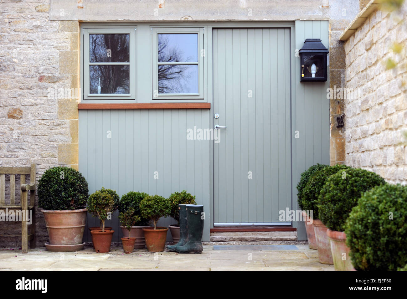 Potted box hedges with wellies by the door to a Cotswold barn