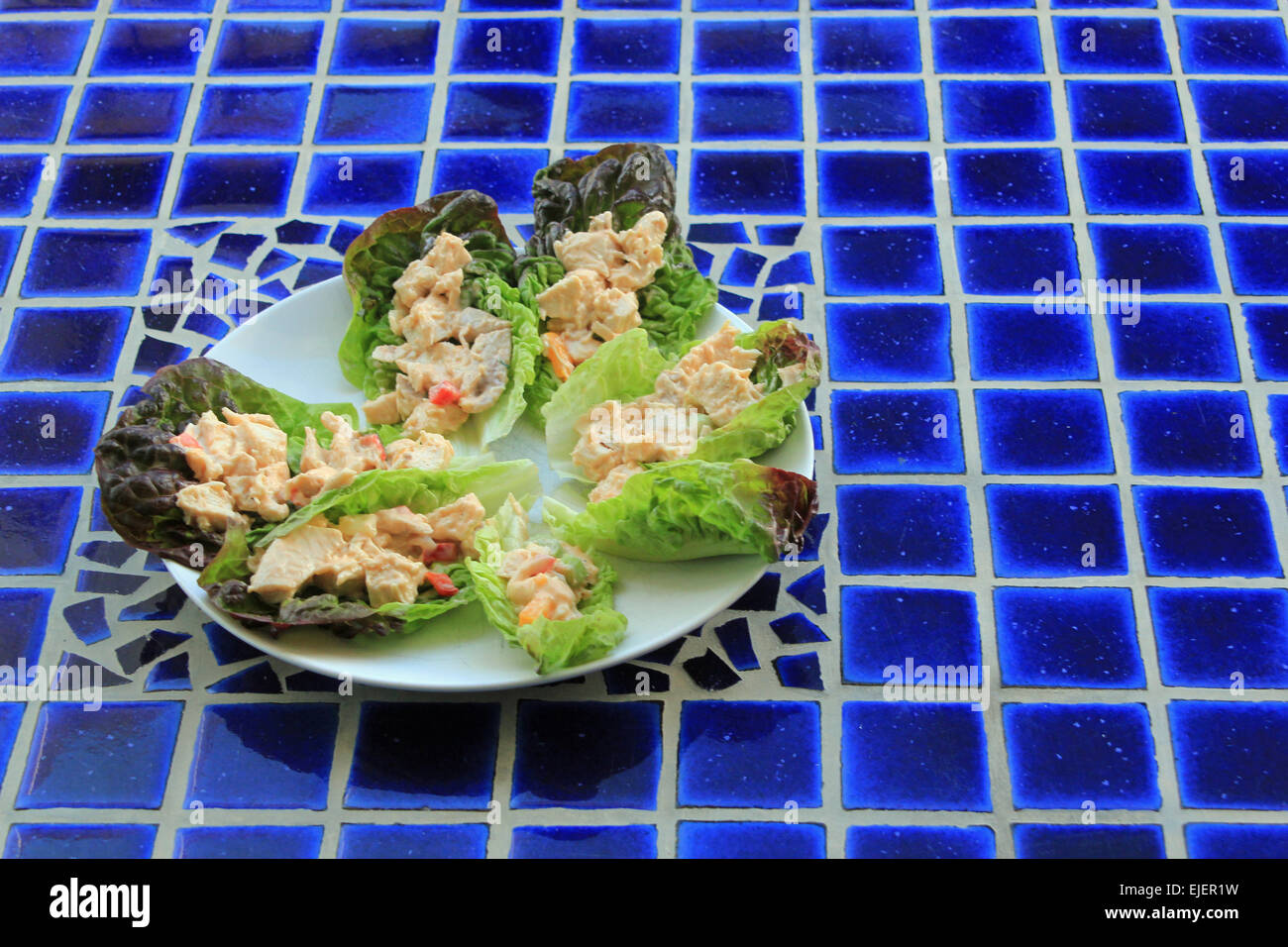 Plate of chicken salad in lettuce wraps on a blue mosaic table symbolizing healthy eating, al fresco eating and summer salads Stock Photo