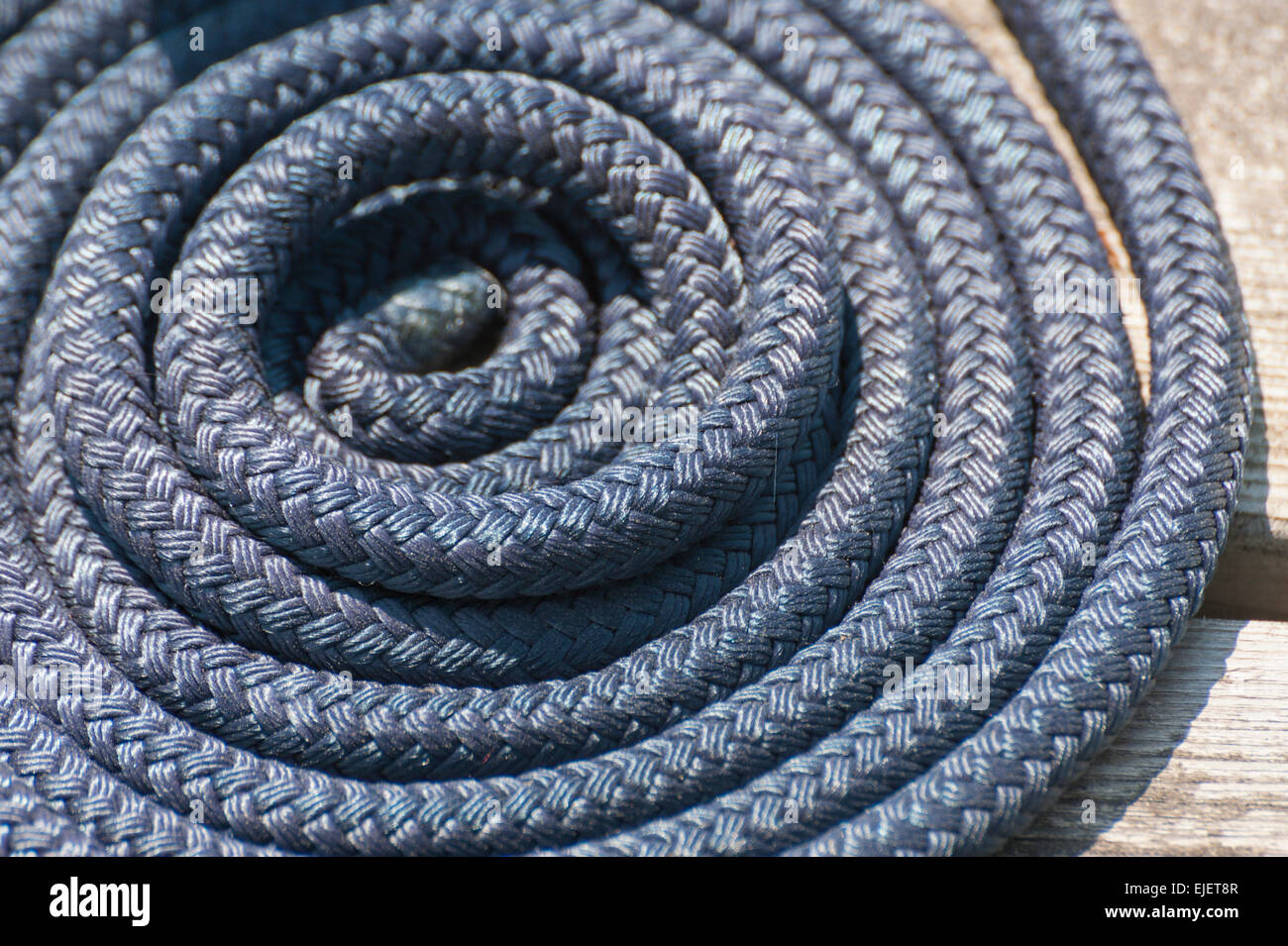 Blue woven rope coiled in a Flemish Flake on a dock at a yacht harbour. Stock Photo