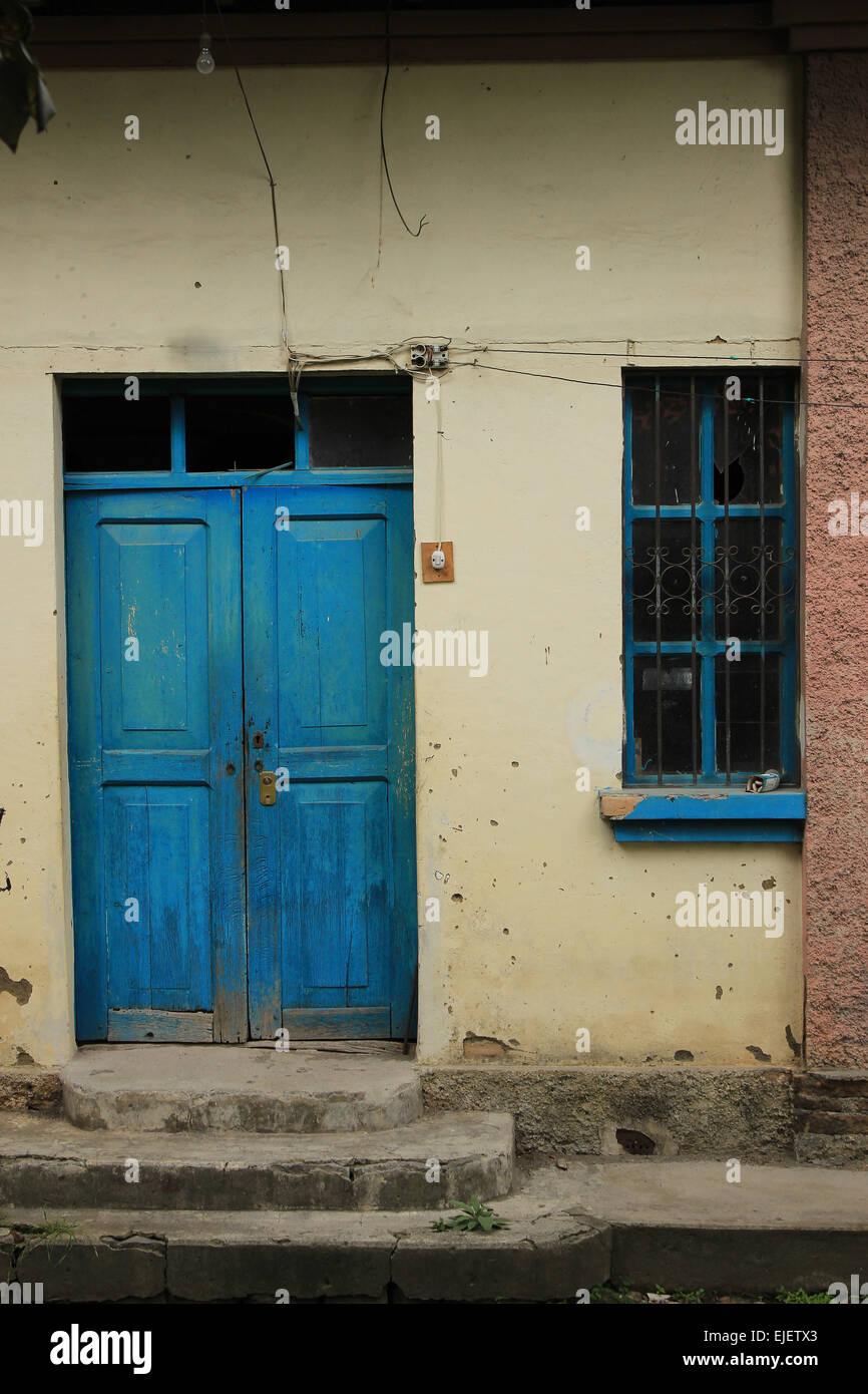 A blue wood door and a window with a blue frame in the concrete wall of a house in Cotacachi, Ecuador Stock Photo