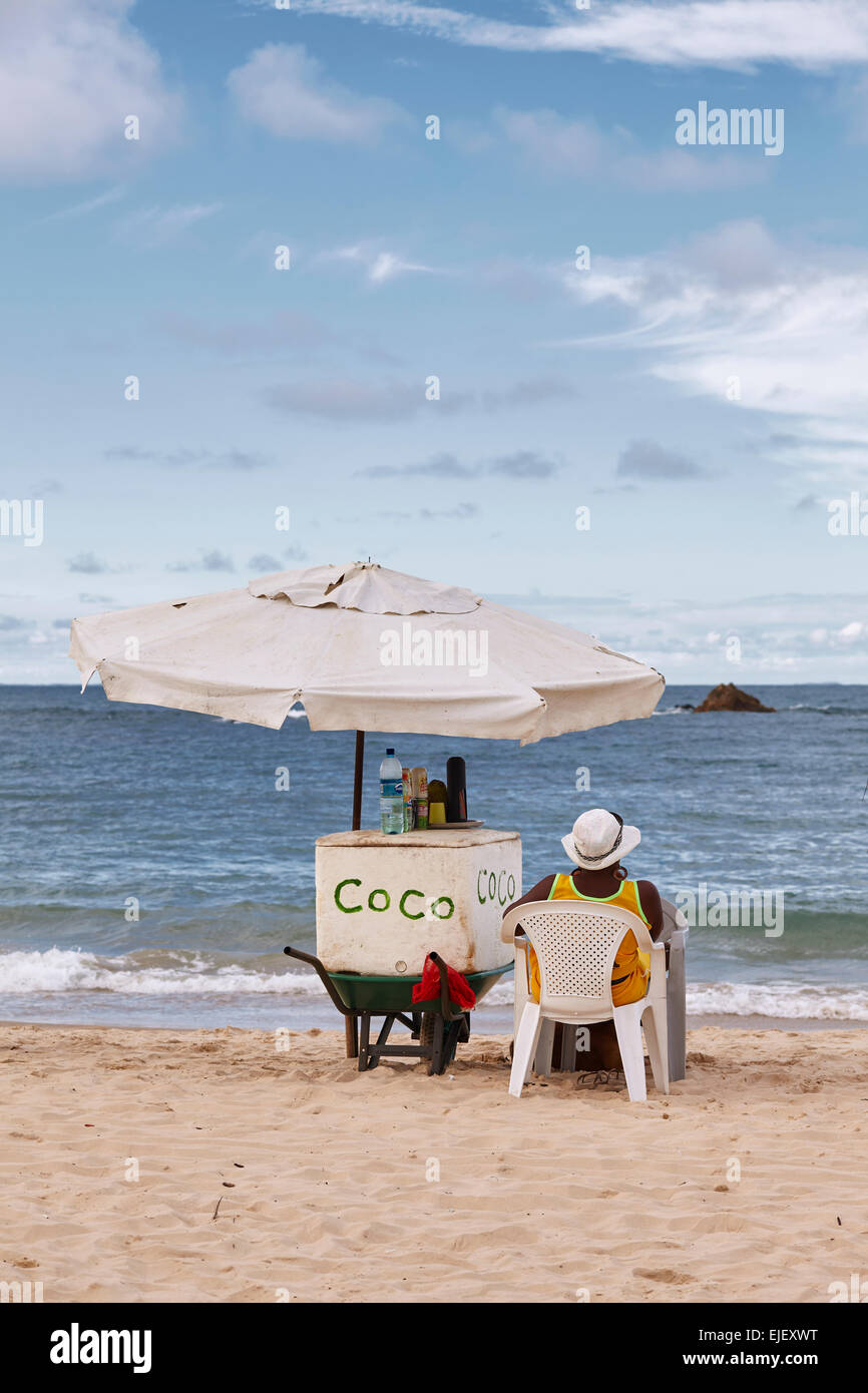 street seller seating on a chair under umbrella on a beach in Morro Sao Paulo, Bahia State, Brazil, against a blue sky Stock Photo