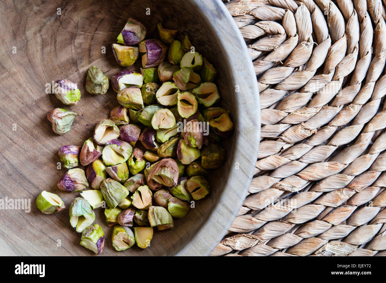 Overhead view of roughly chopped  pistachios in an olive wood bowl on a rush mat. Stock Photo