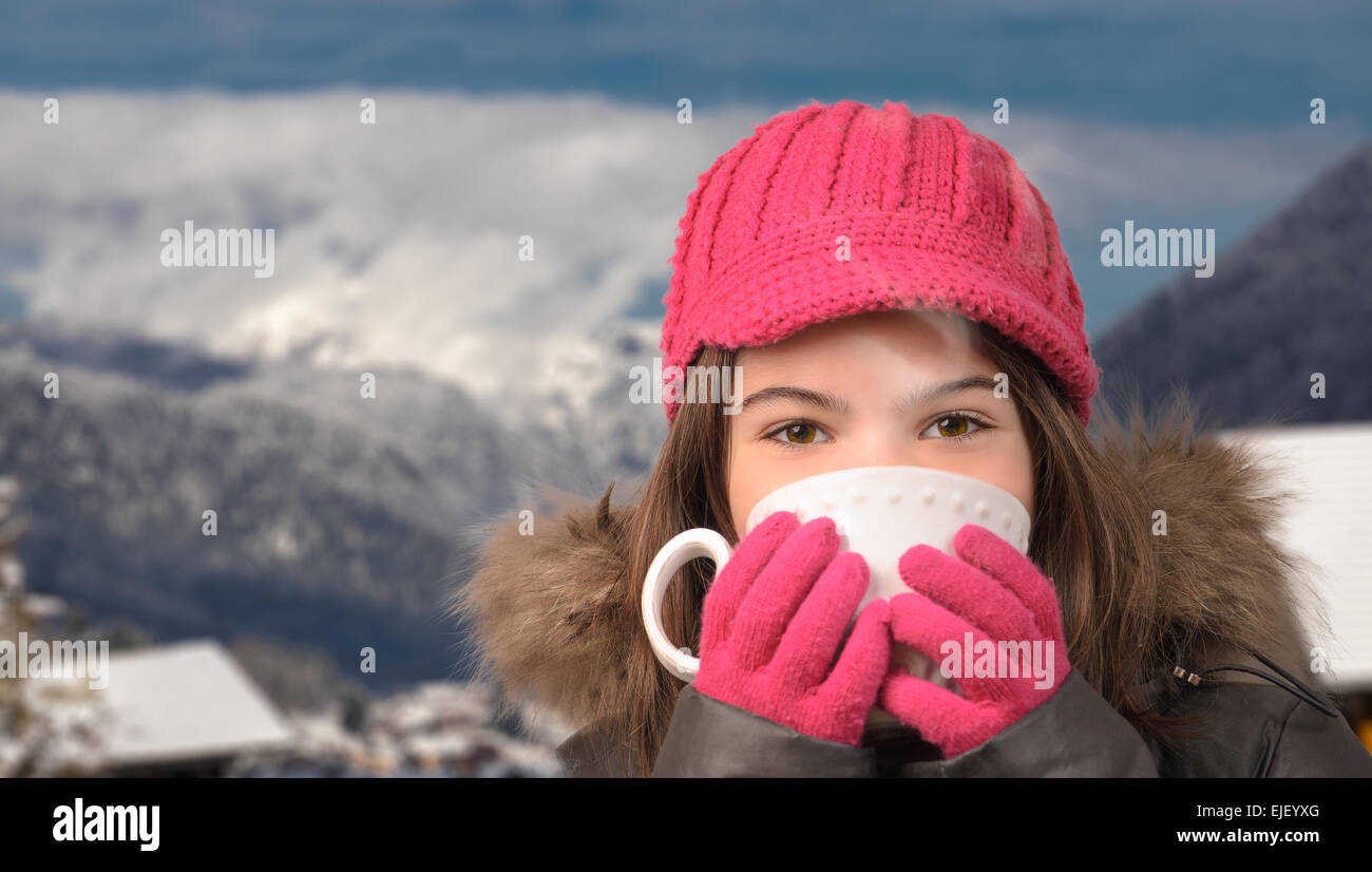 Cute girl with a cup of tea in the snowy mountain village, smoke, vapor, from hot tea with mountain peak in the distance Stock Photo