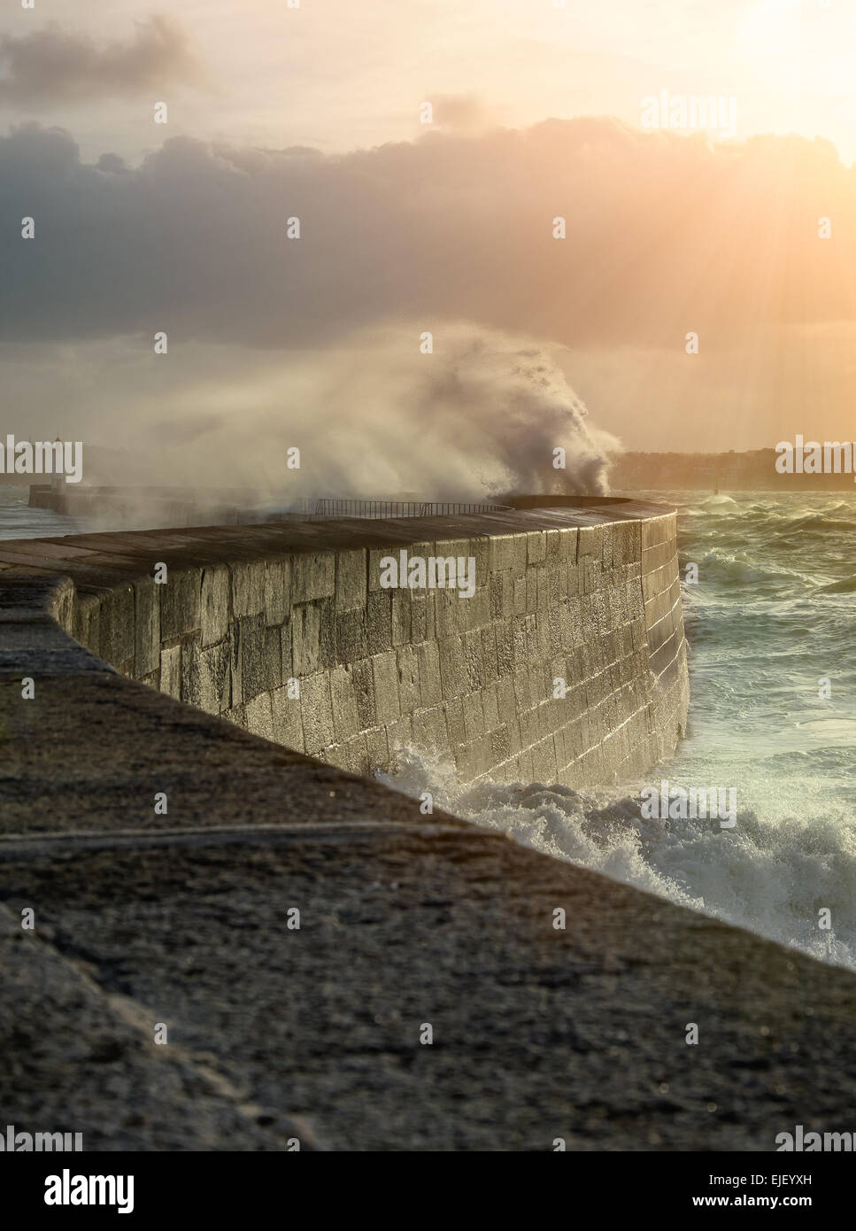 Big waves crushing on curved stone pier, on stormy weather with vivid sunset, big tide, Saint Malo, France. Stock Photo