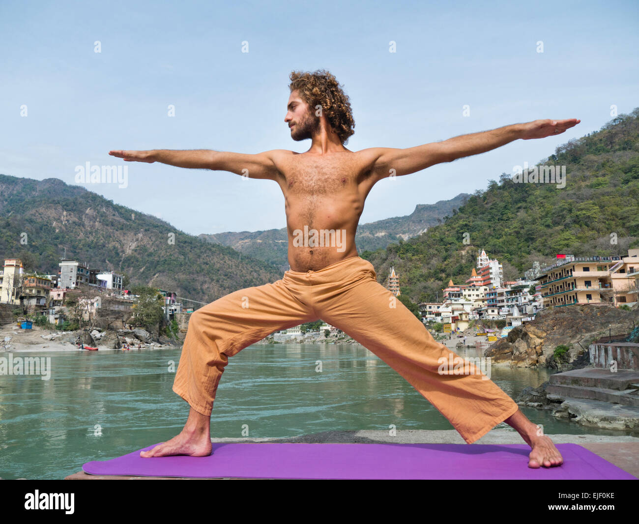 A man practicing yoga warrior pose by the Ganges river in Rishikesh India Stock Photo