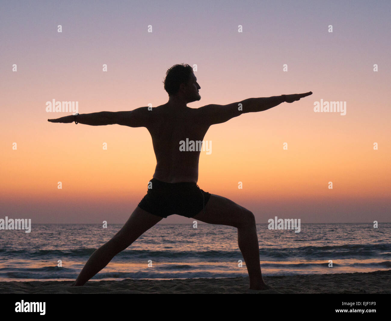 A man practicing yoga warrior pose on a beach Stock Photo
