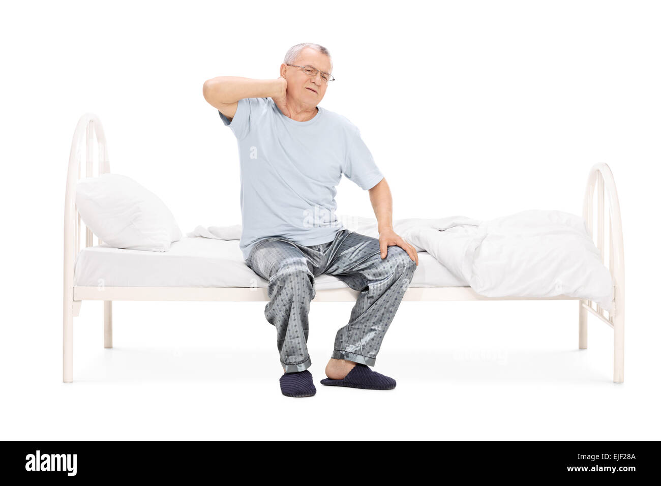 Senior in pajamas feeling pain in the neck seated on a bed isolated on white background Stock Photo