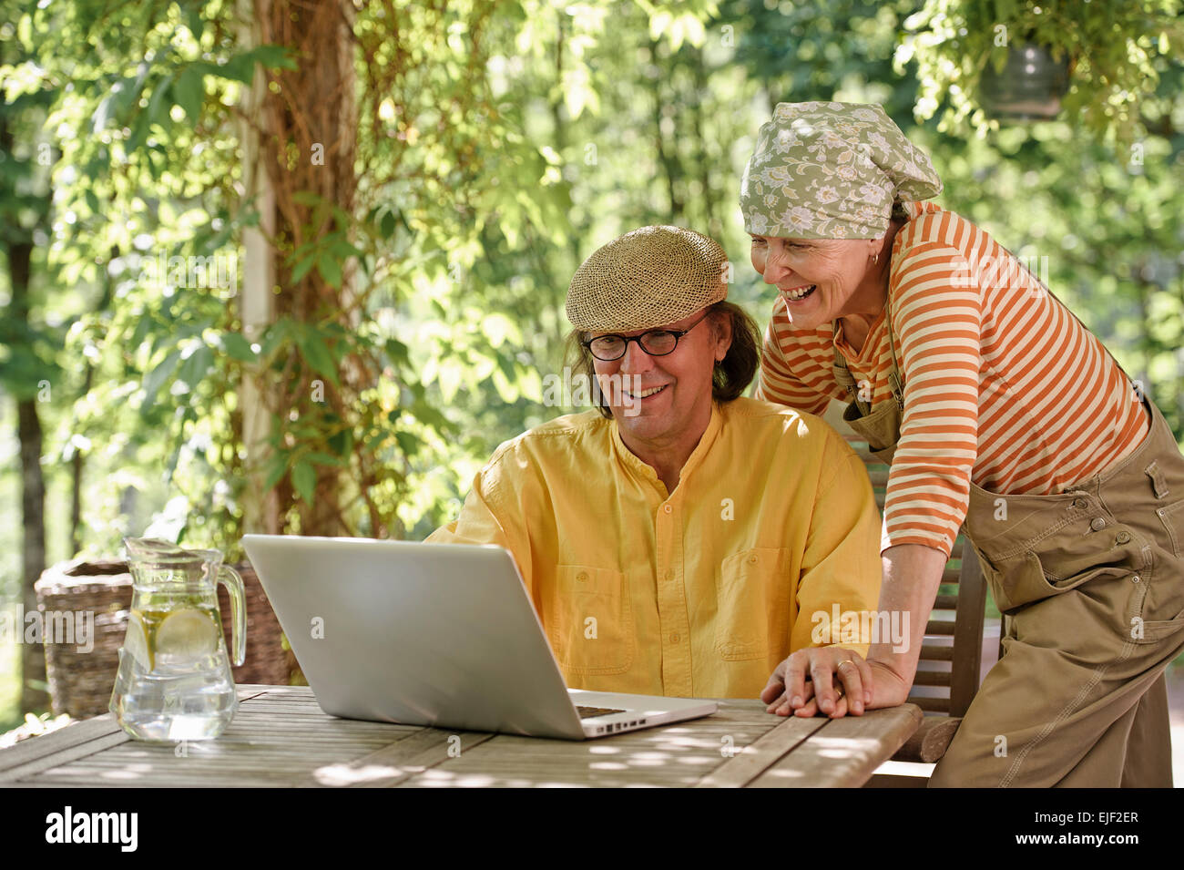 Senior couple outdoors with a laptop, They're looking at the computer. Possibly having a wireless video call with grandchildren. Stock Photo