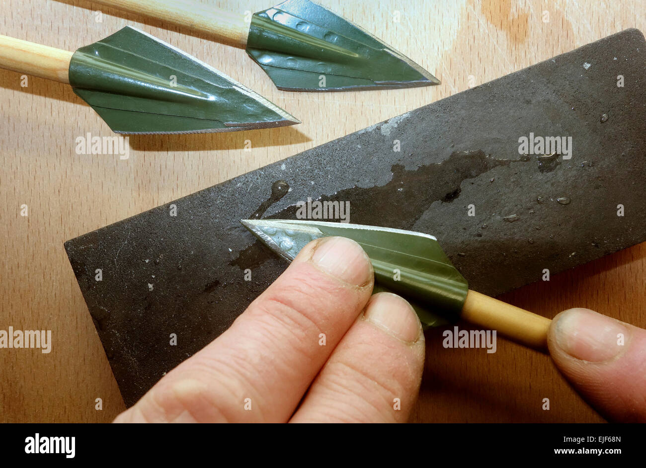 Broadhead arrowhead on wooden shaft are in process of sharpening for big game hunt purpose. Stock Photo