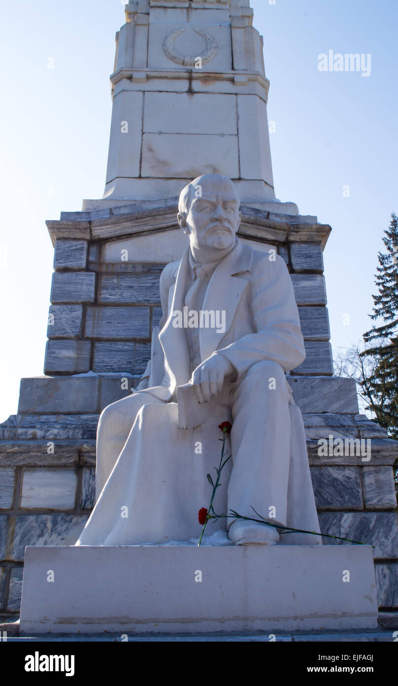 Lenin sitting down in a statue form with white carving and red carnation flowers Stock Photo