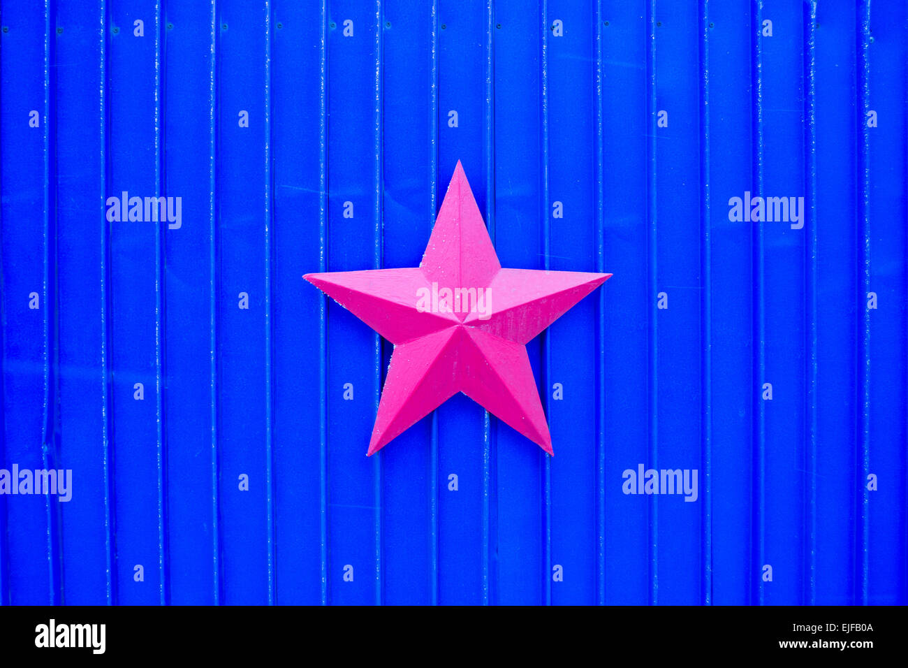 A single red metal star attached to a bright blue corrugated metal gate Stock Photo