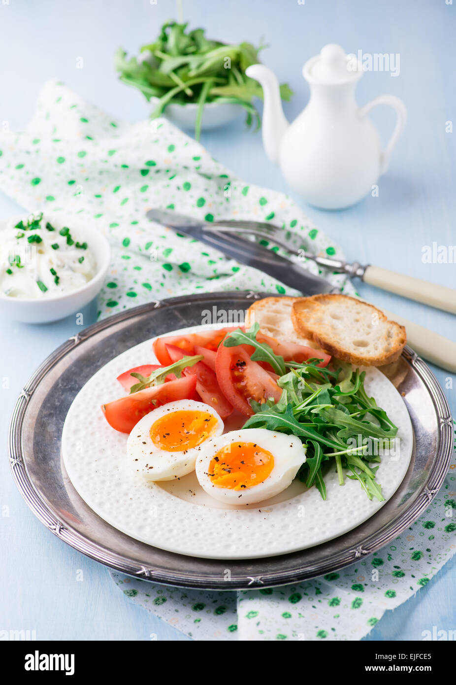 Breakfast with soft-boiled egg, arugula, soft cheese and tomatoes, selective focus Stock Photo