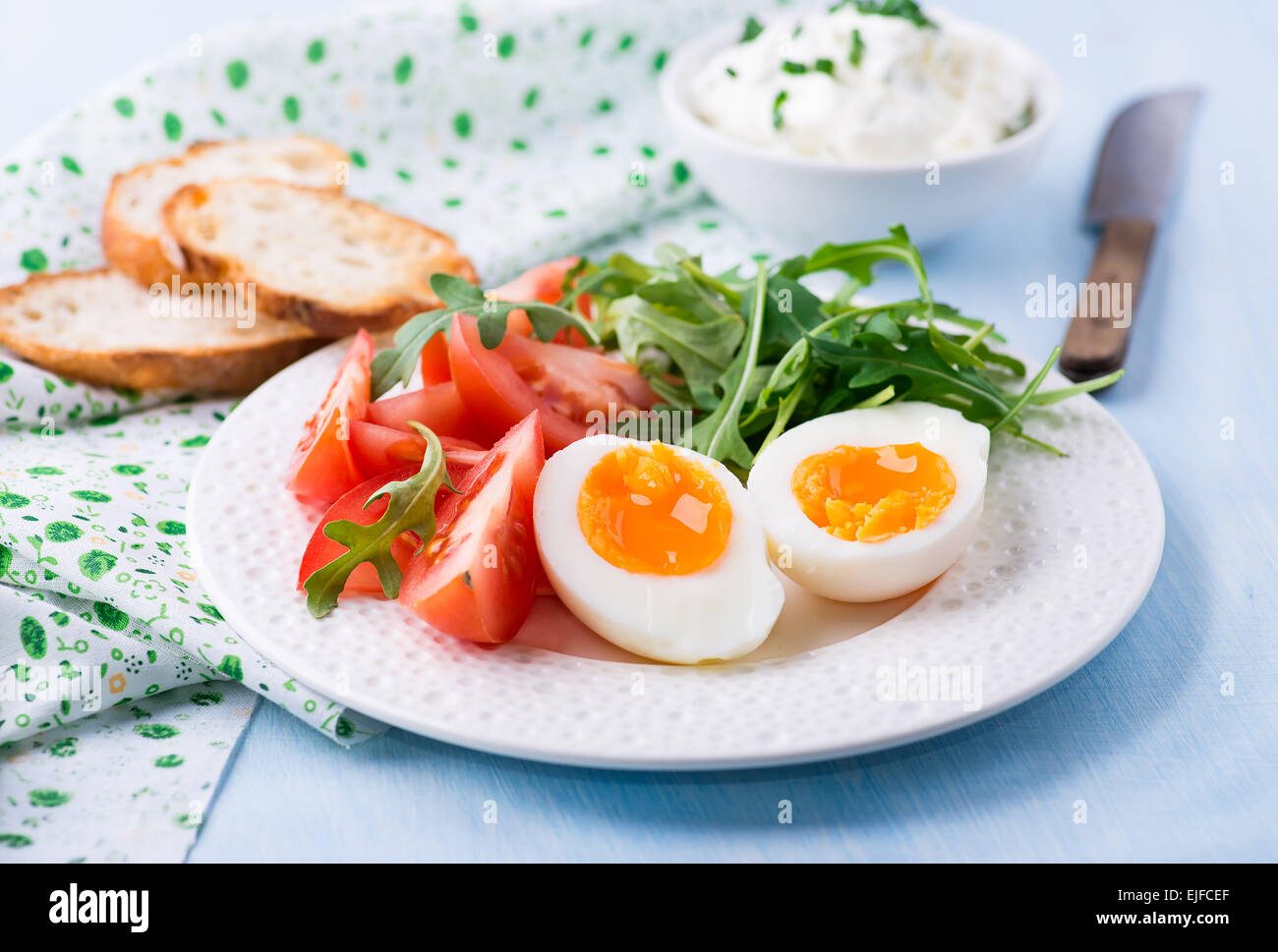 Breakfast with soft-boiled egg, arugula, soft cheese and tomatoes, selective focus Stock Photo