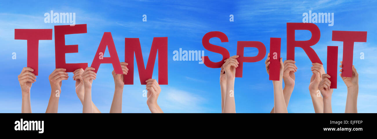Many Caucasian People And Hands Holding Red Letters Or Characters Building The English Word Team Spirit On Blue Sky Stock Photo