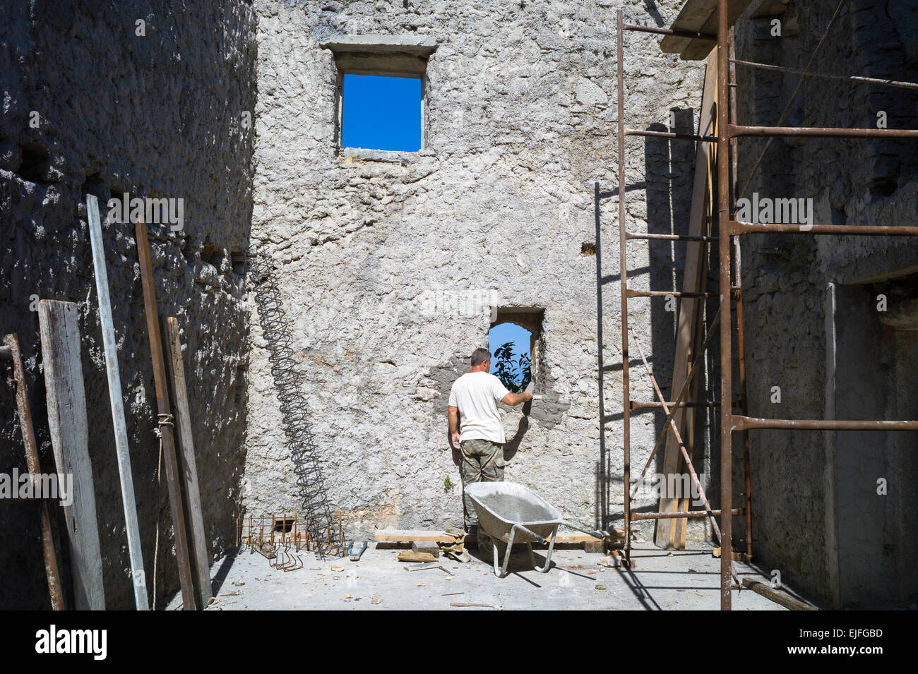 Builder doing masonry building work restoring derelict old stone house in ruins in village of Old Perithia - Palea Perithea, Cor Stock Photo