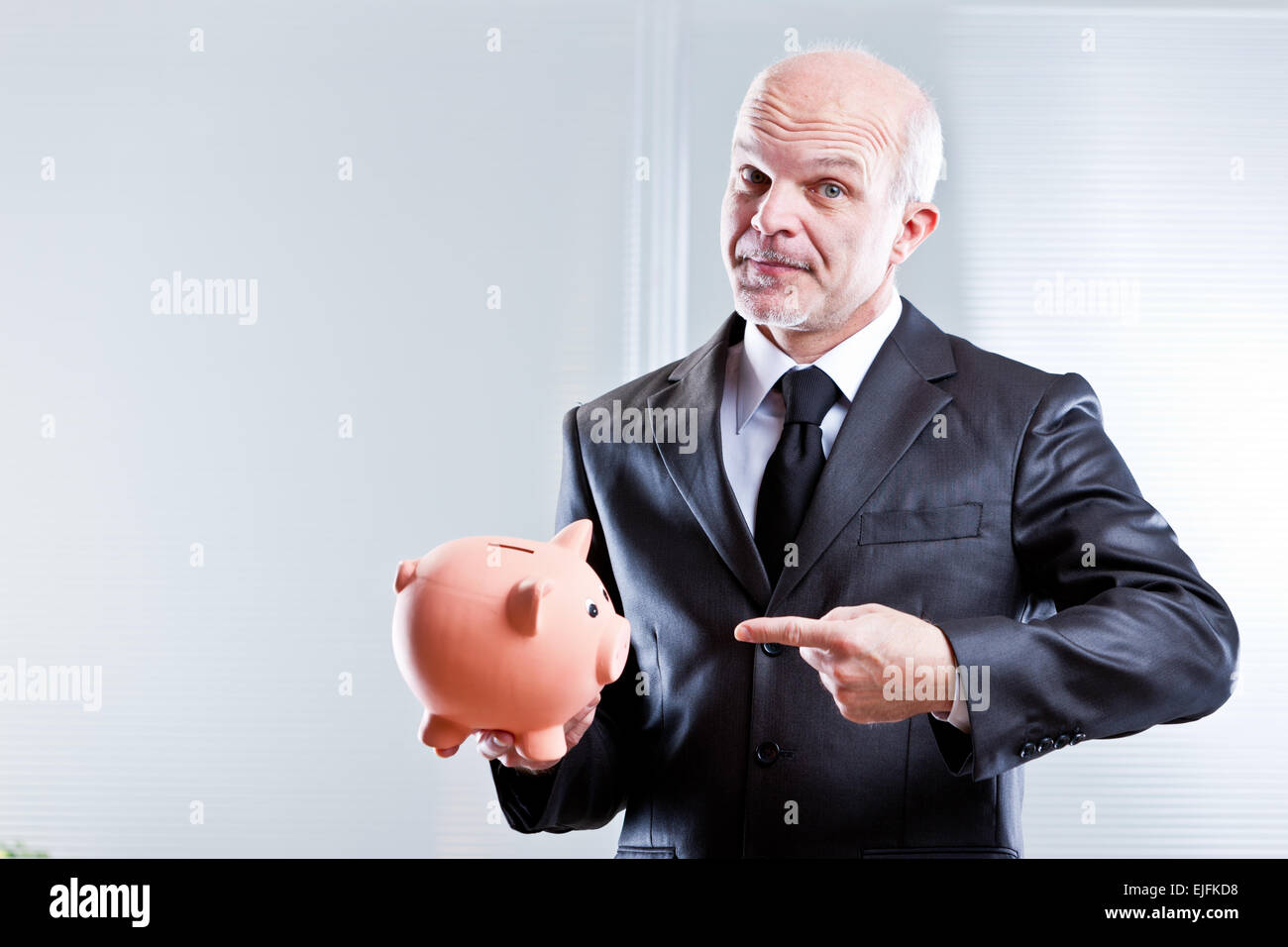business man pointing out a piggy bank meaning you have to save Stock