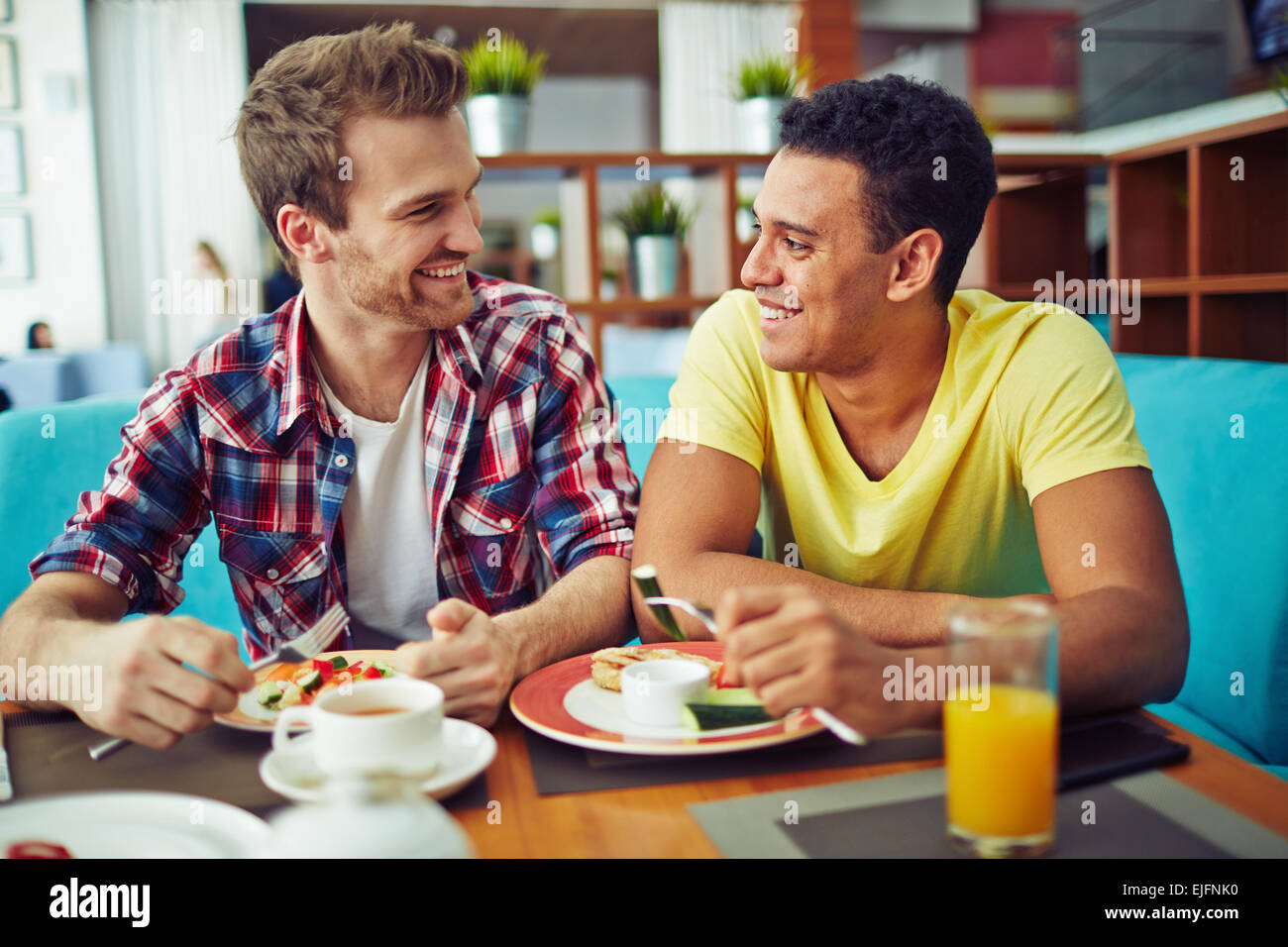 Two men eating and looking at each other Stock Photo