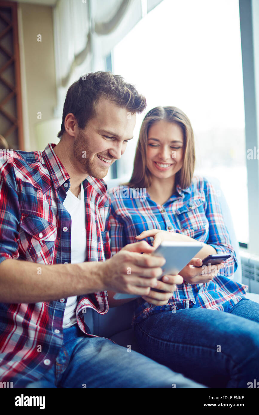 Smiling boy and girl looking at their digital devices Stock Photo
