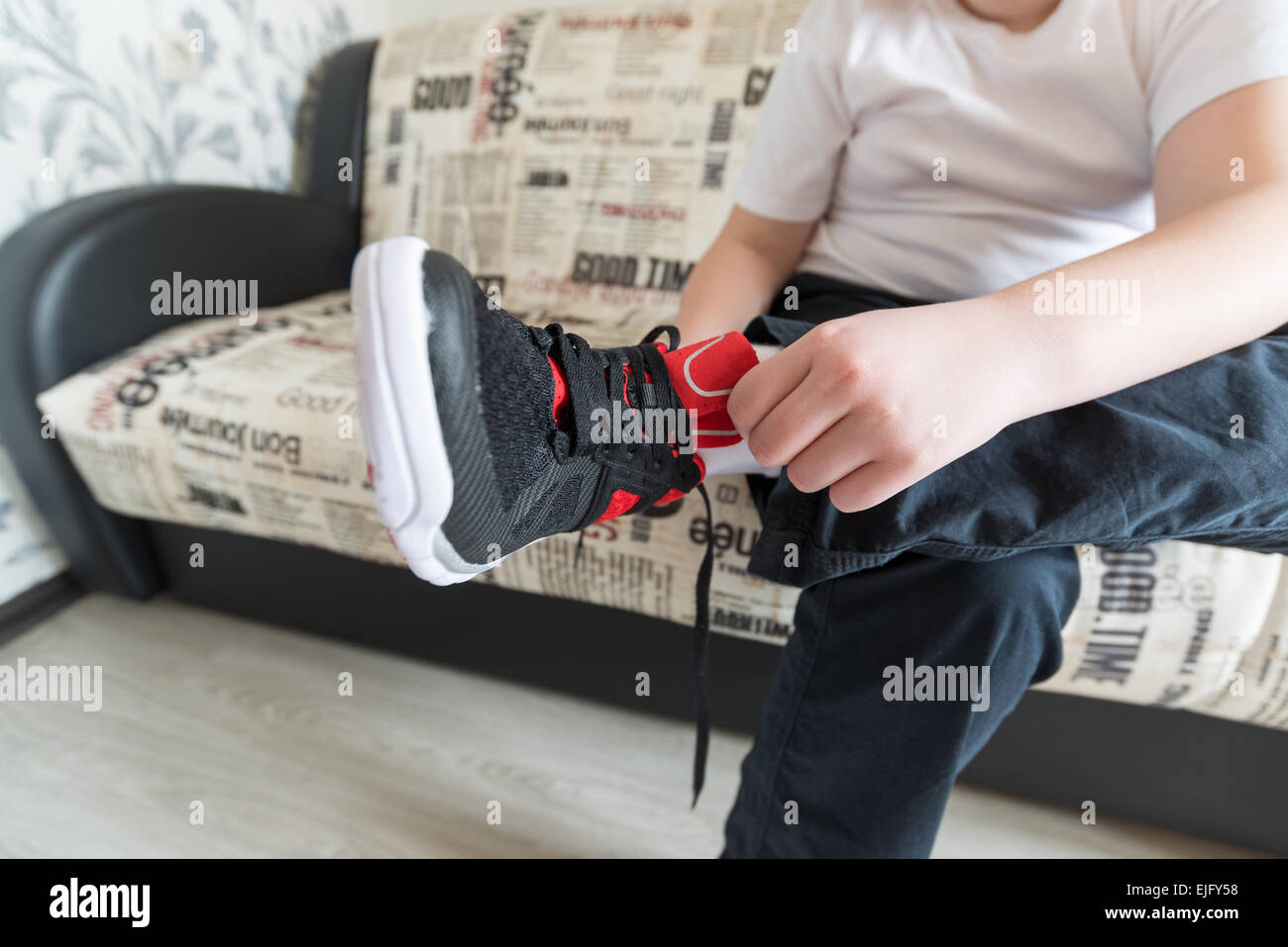 The boy wears running shoes sitting on a sofa in  room Stock Photo