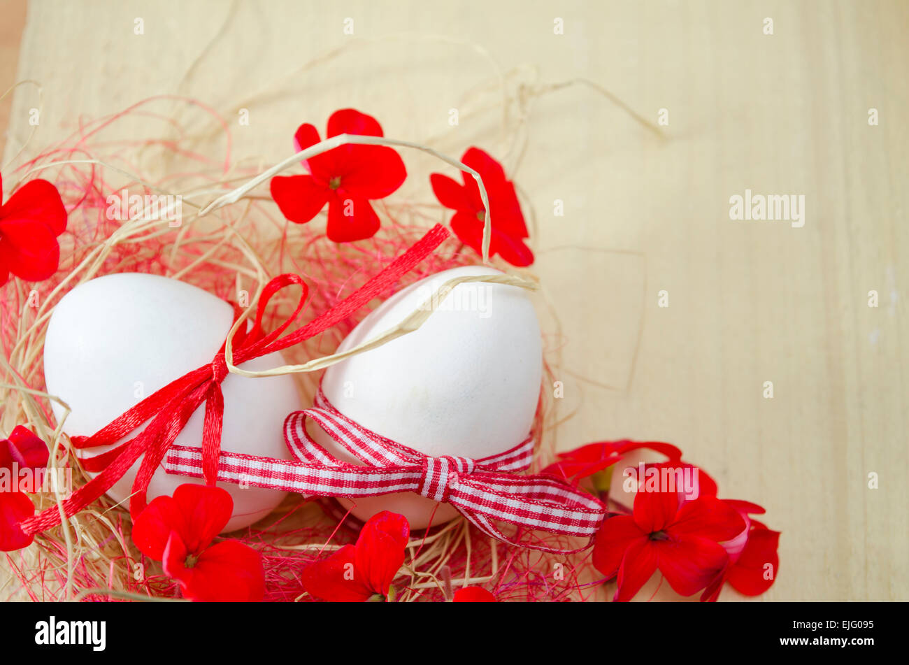 Two white eggs with ribbons attached lying in a nest with two red flowers Stock Photo