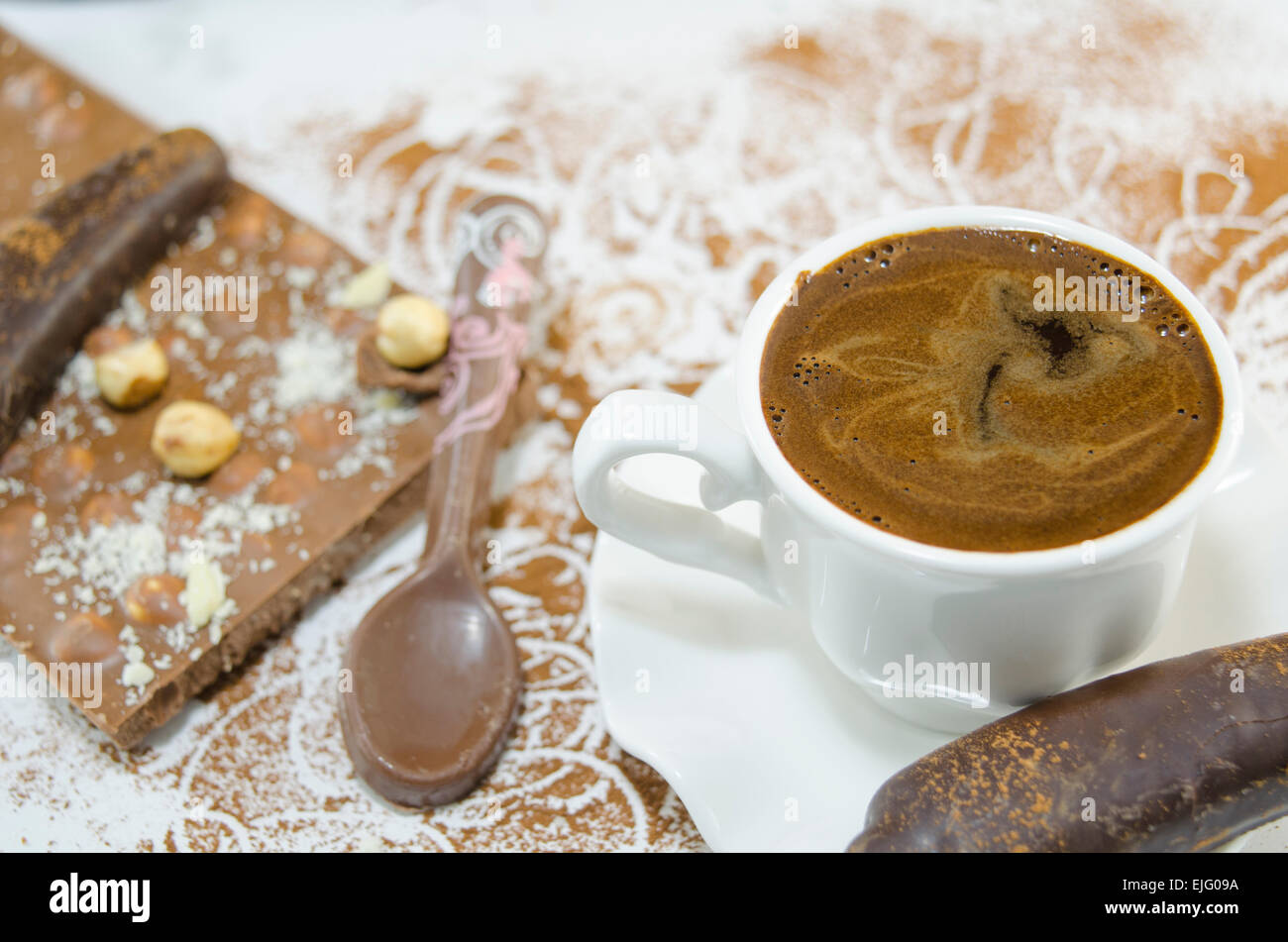 Cup of coffee with a subtly heart shaped foam decorated with flowers and banana shaped chocolate Stock Photo