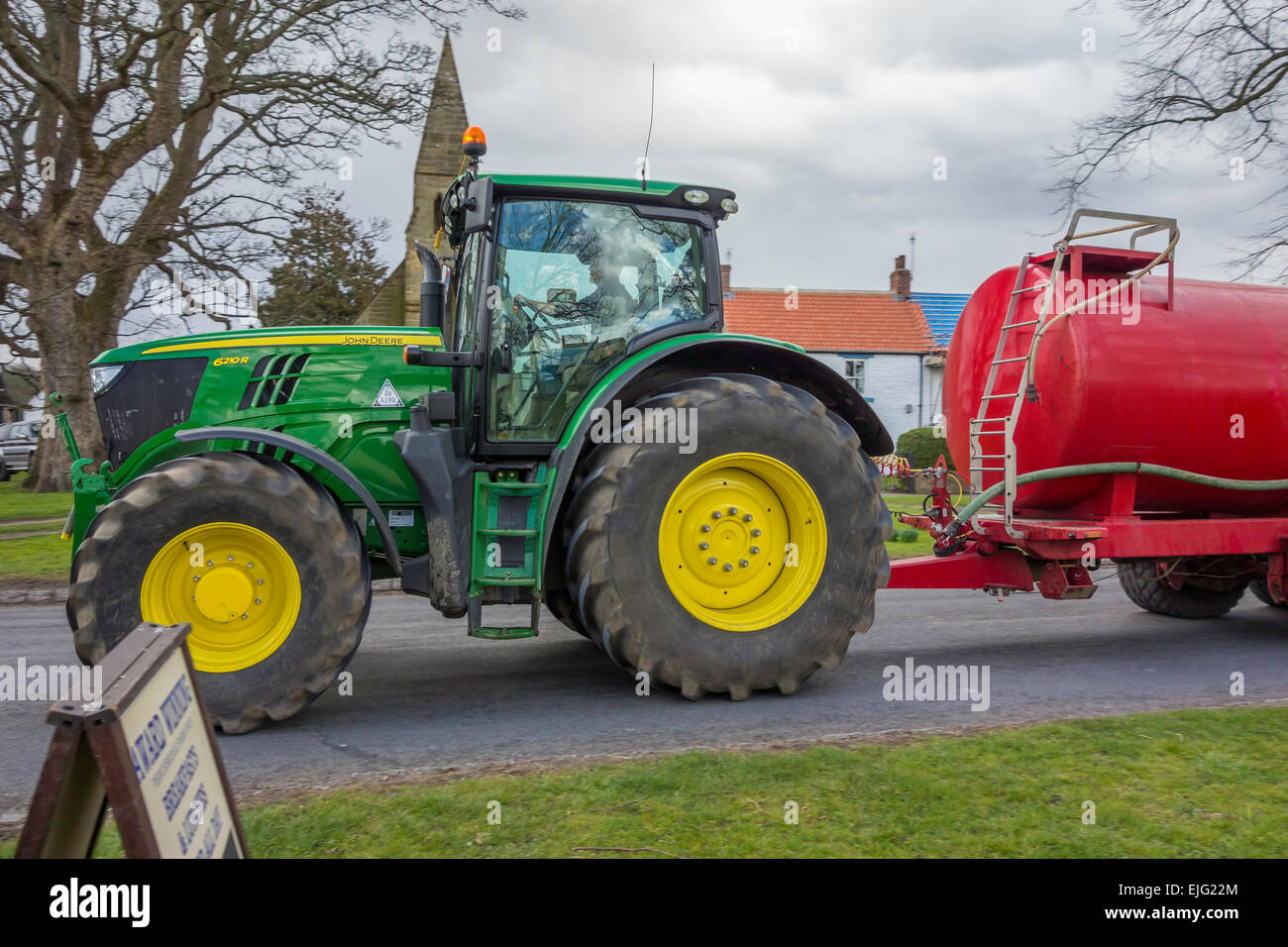 A John Deere 6210R agricultural tractor towing a tank trailer through a village in County Durham England UK Stock Photo Alamy