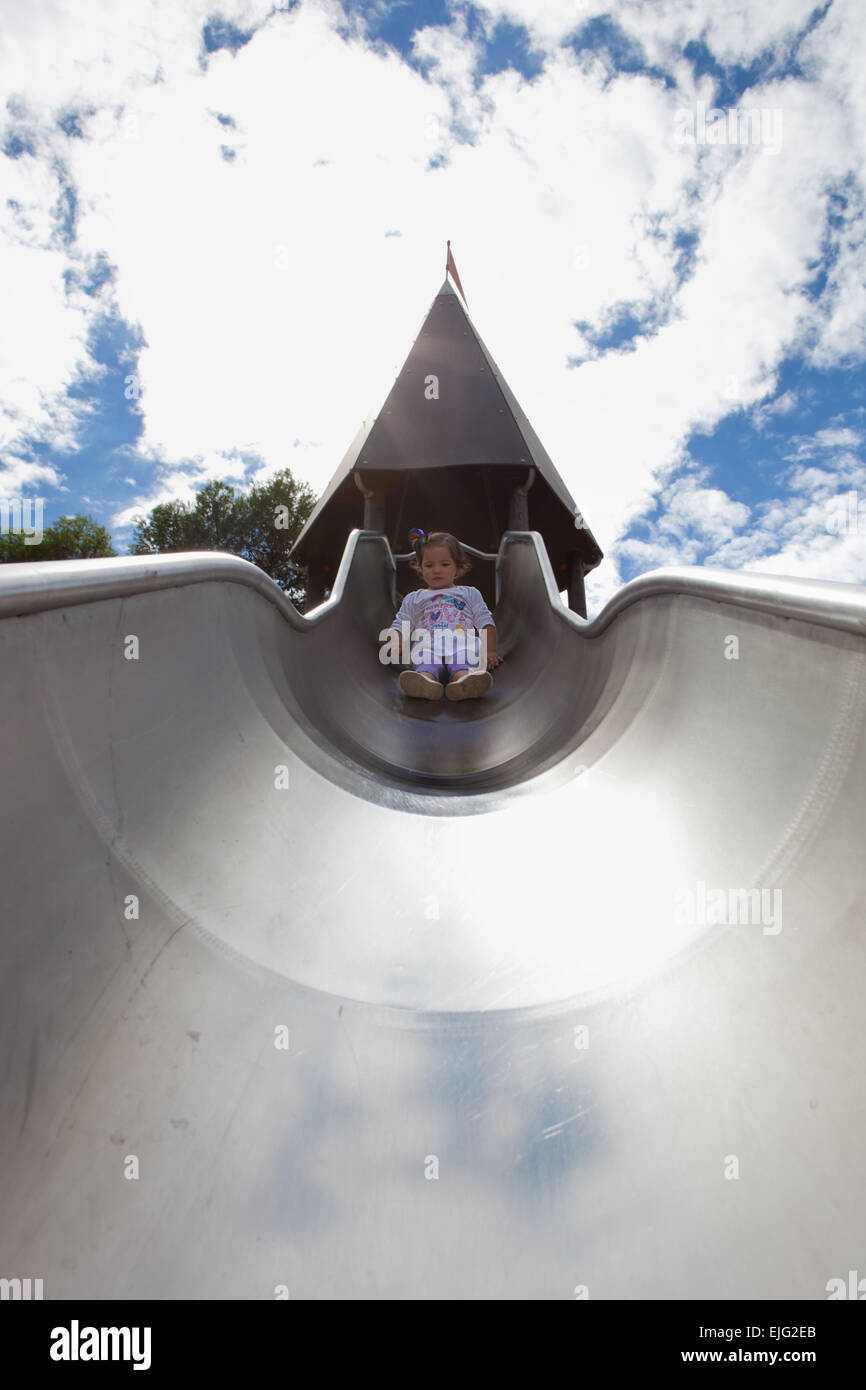 Beautiful little girl on the top of the metal playground slide Stock Photo