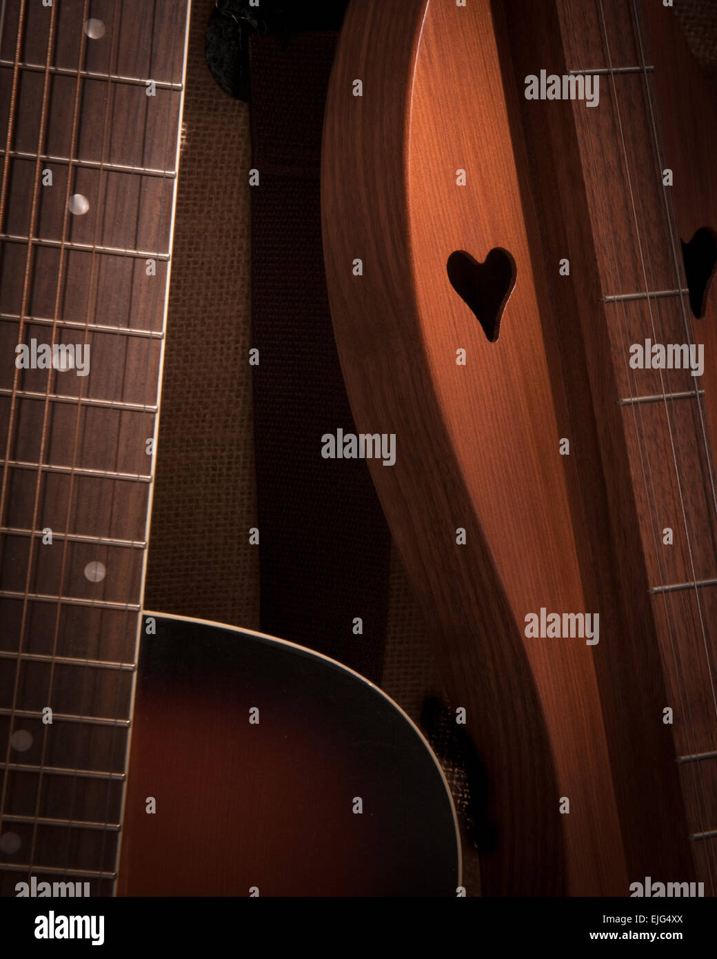 Acoustic resonator and a beautifully carved dulcimer with heart cut-outs rest together in this close-up shot taken against a burlap background. Stock Photo