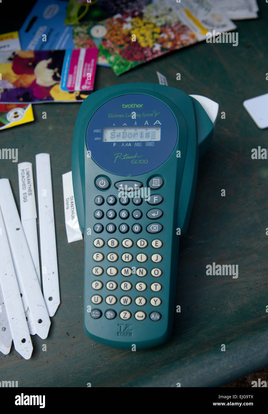 Printing labels for garden plants, using a Brother hand printer in a greenhouse. On the bench in a potting tray. Stock Photo