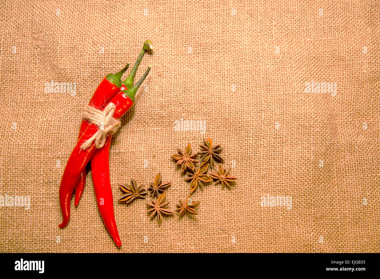 Three Chile peppers tied with a rope and star anise fruits on old cloth ...