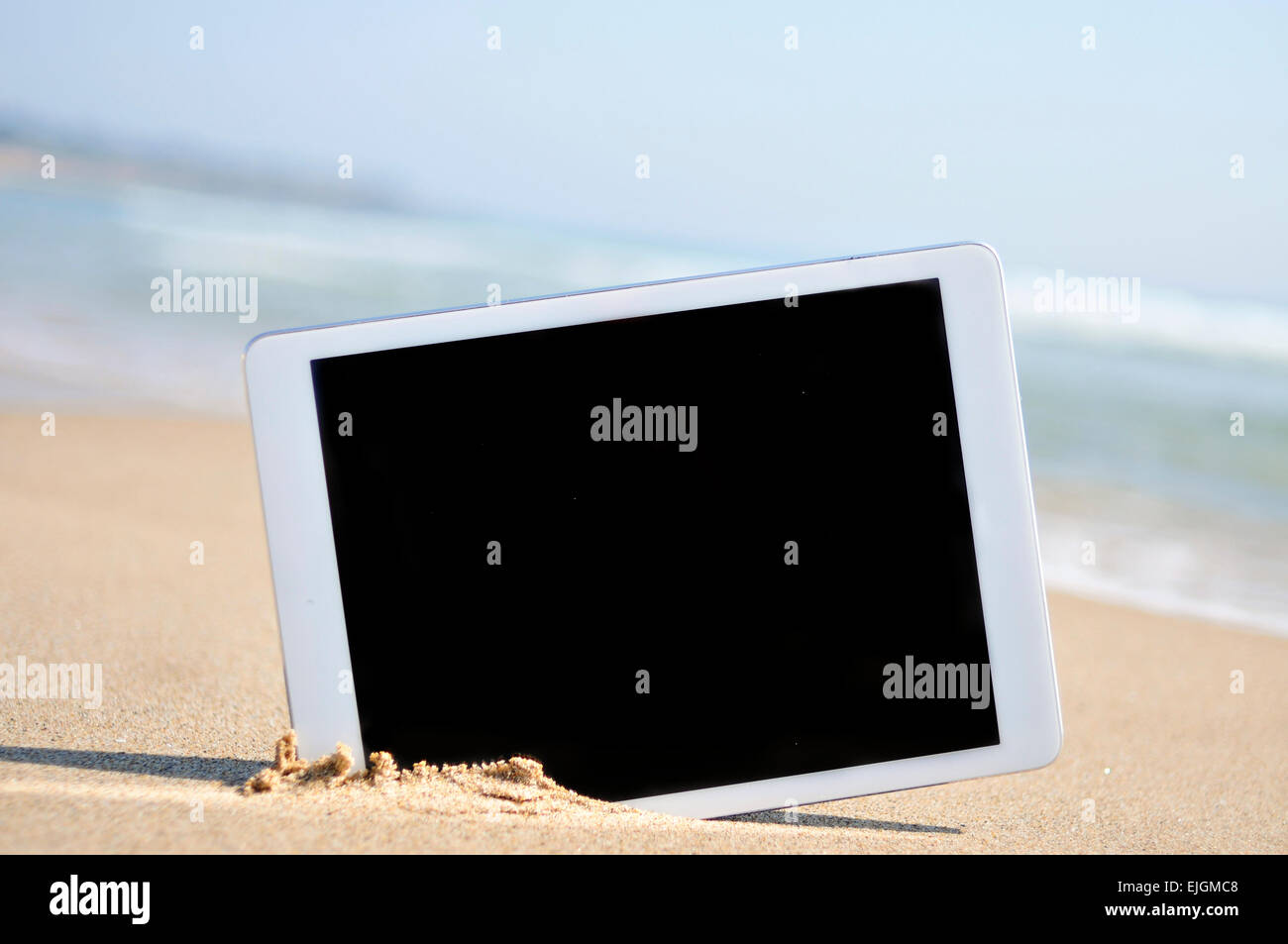 a tablet computer with a black blank space in the screen, in the sand ...