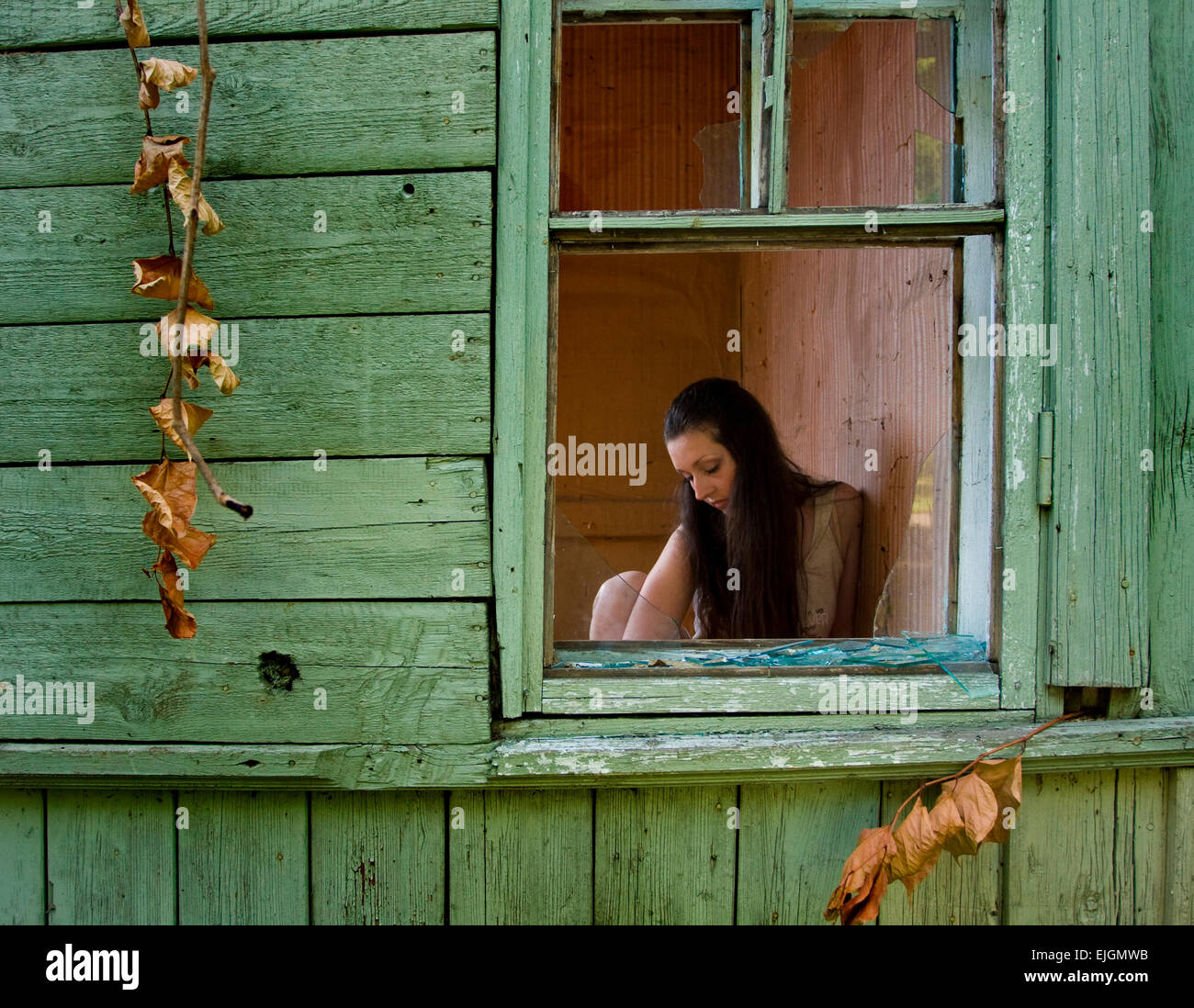 sad beautiful girl with long black hair in the window of an old house Stock Photo