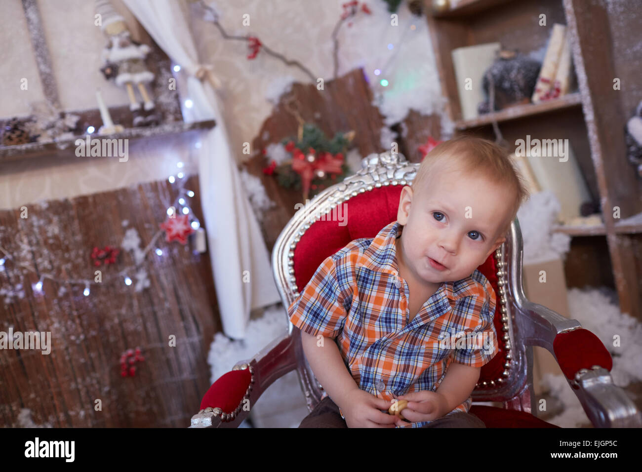 active, cheerful kid is sitting in a chair near the Christmas tree Stock Photo