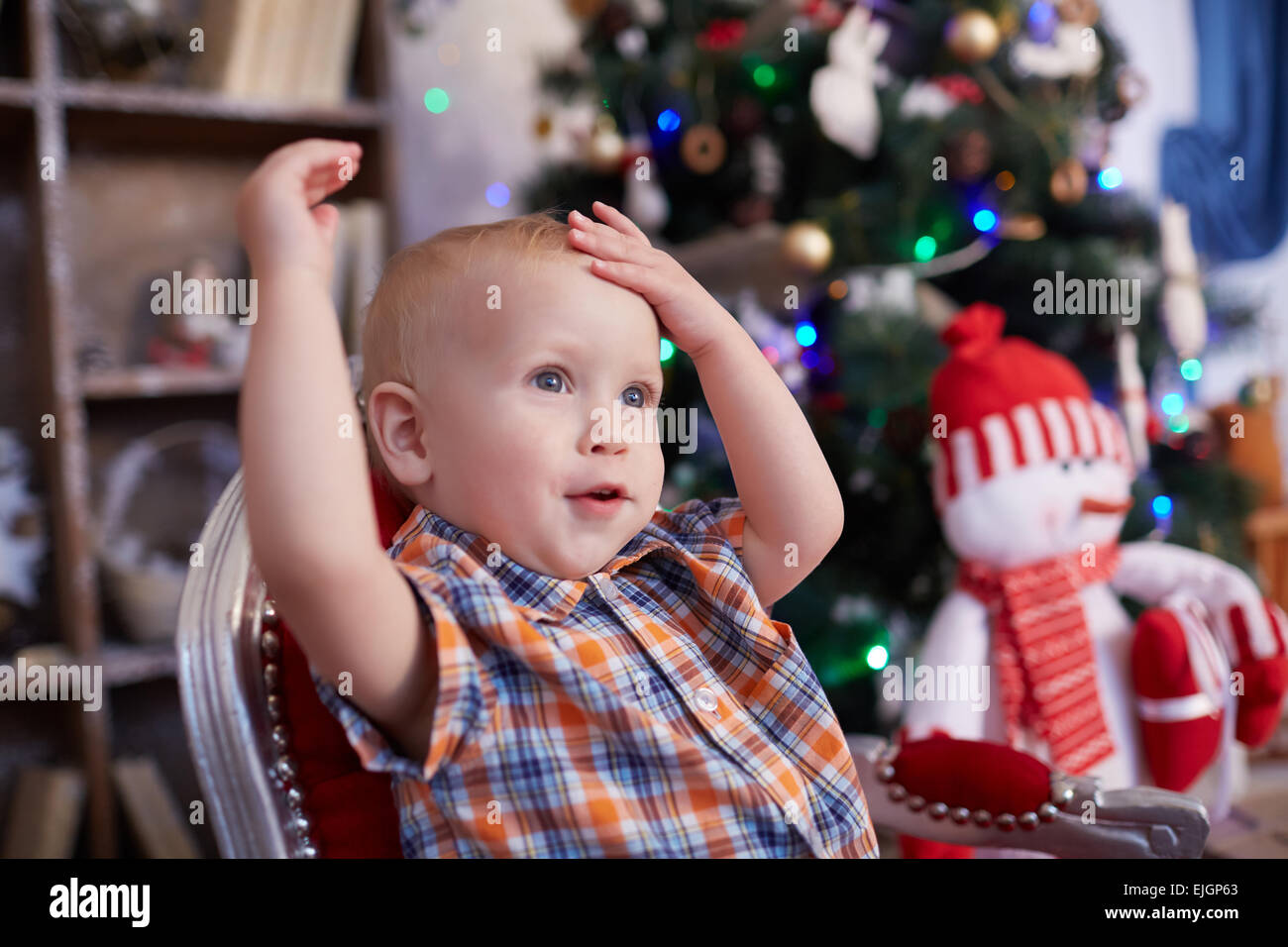 active, cheerful kid is sitting in a chair near the Christmas tree Stock Photo