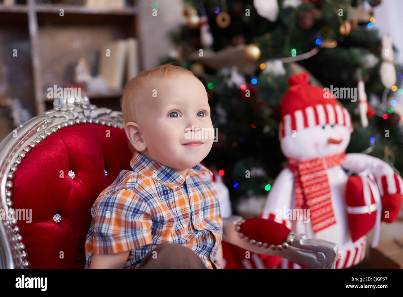 active, cheerful kid is sitting in a chair near the Christmas tree Stock Photo