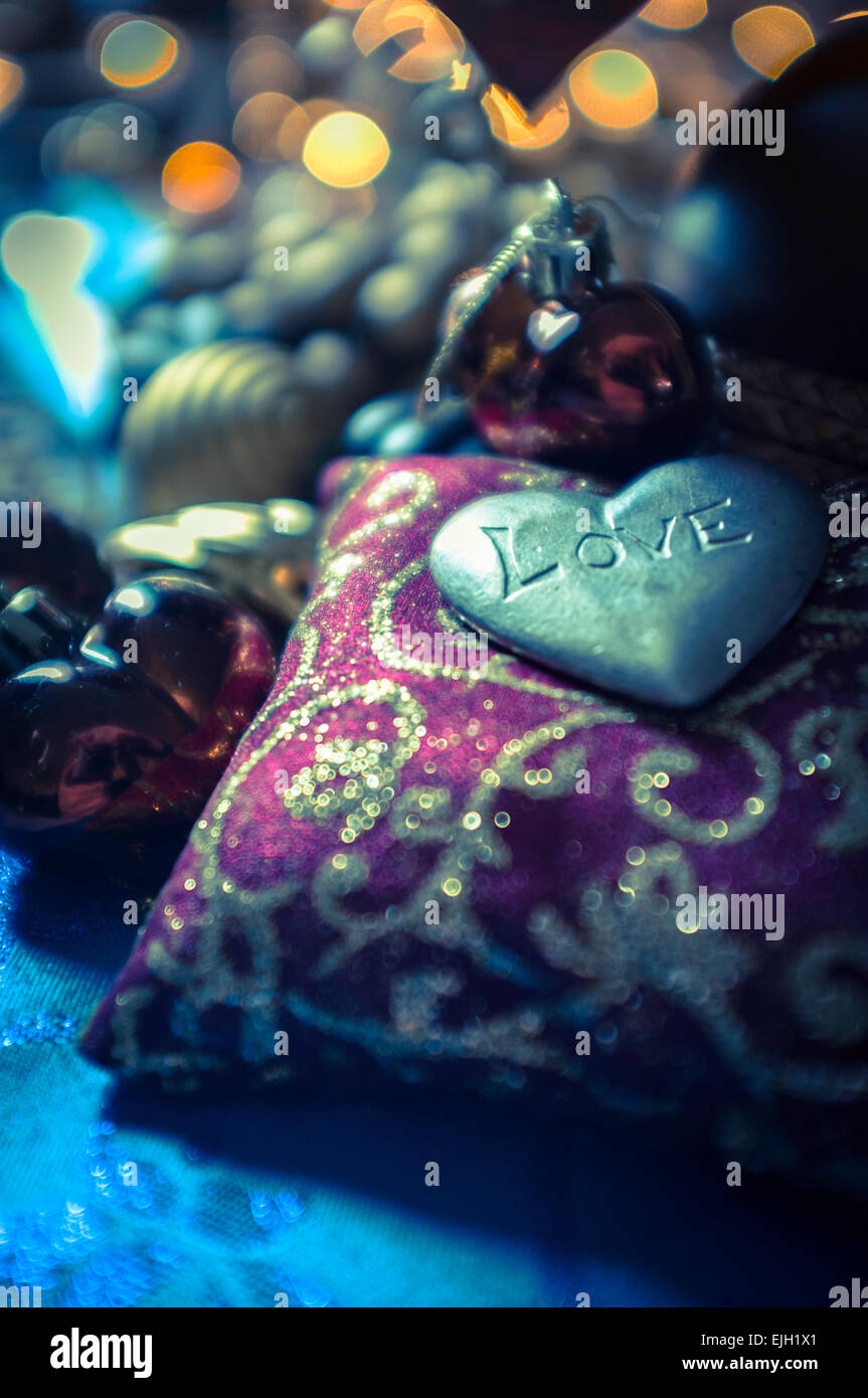 metallic heart shaped engraved love token sitting on small cushion amongst various baubles and decorations Stock Photo