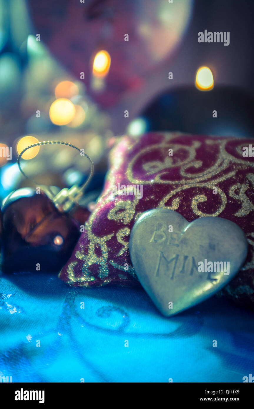 metallic heart shaped engraved love token sitting on small cushion amongst various baubles and decorations Stock Photo