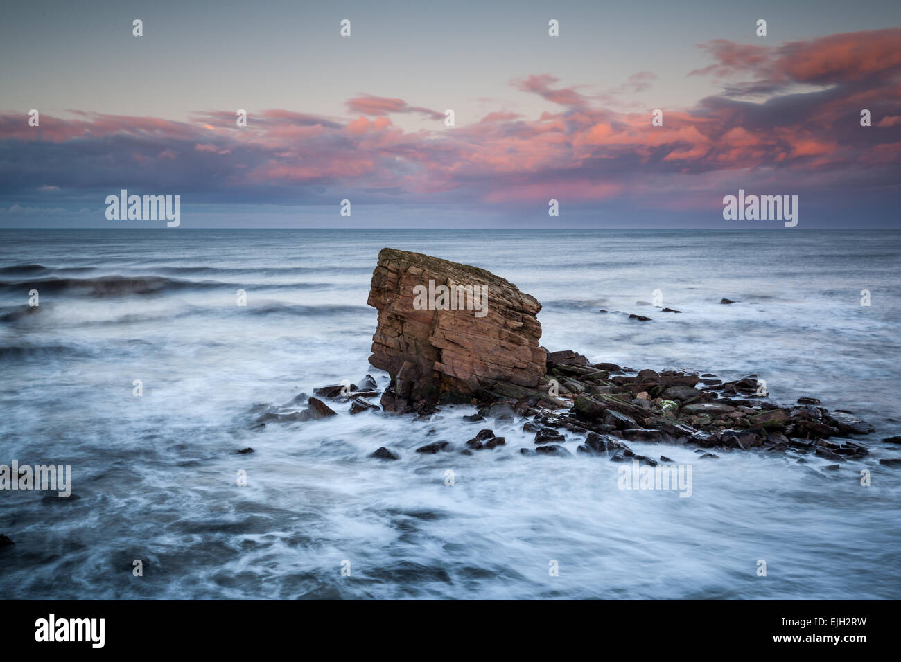 Charlie's Garden sea stack at Colywell Bay, Northumberland at sunset and high tide with rough seas crashing around the rocks. Stock Photo