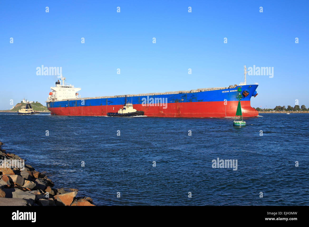 A large cargo ship entering the Hunter River on its way to the Port of Newcastle, NSW, Australia. There are two tugs assisting. Stock Photo