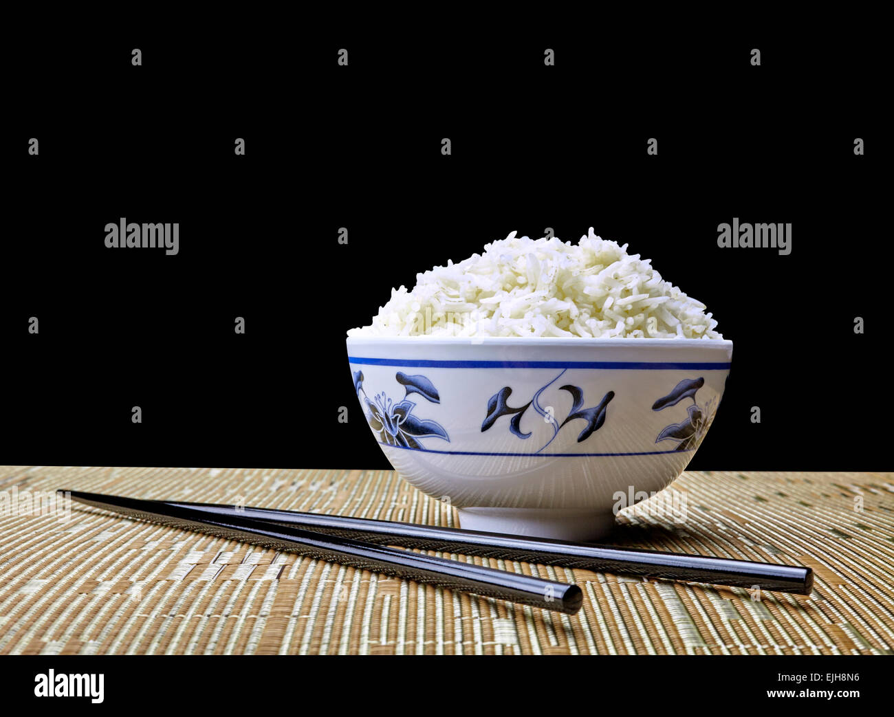 Bowl of Cooked  Natural Organic Jasmine Rice in Oriental Bowl on Place Setting with Chopsticks on Black Background Stock Photo