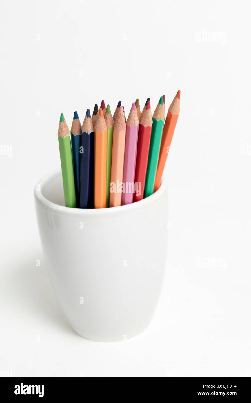 A group of multi colored pencils in a white cup on an isolated background Stock Photo
